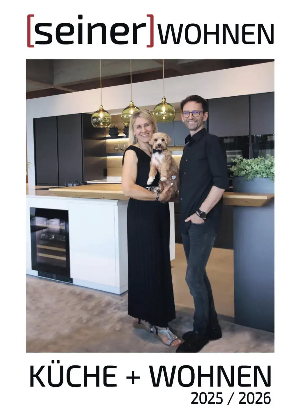 Titelblatt „Küche + Wohnen 2025 / 2026“ mit einer Frau und einem Mann samt Hund in einer Küche mit goldenen Pendelleuchten und Weinkühlschrank