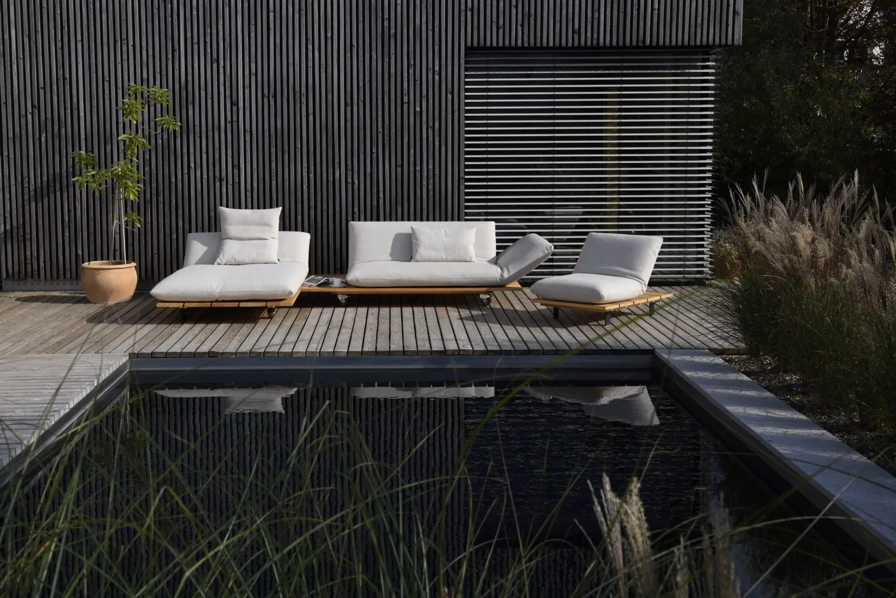 Outdoor-Lounge Akito am Pool vor einer dunklen Holzfassade