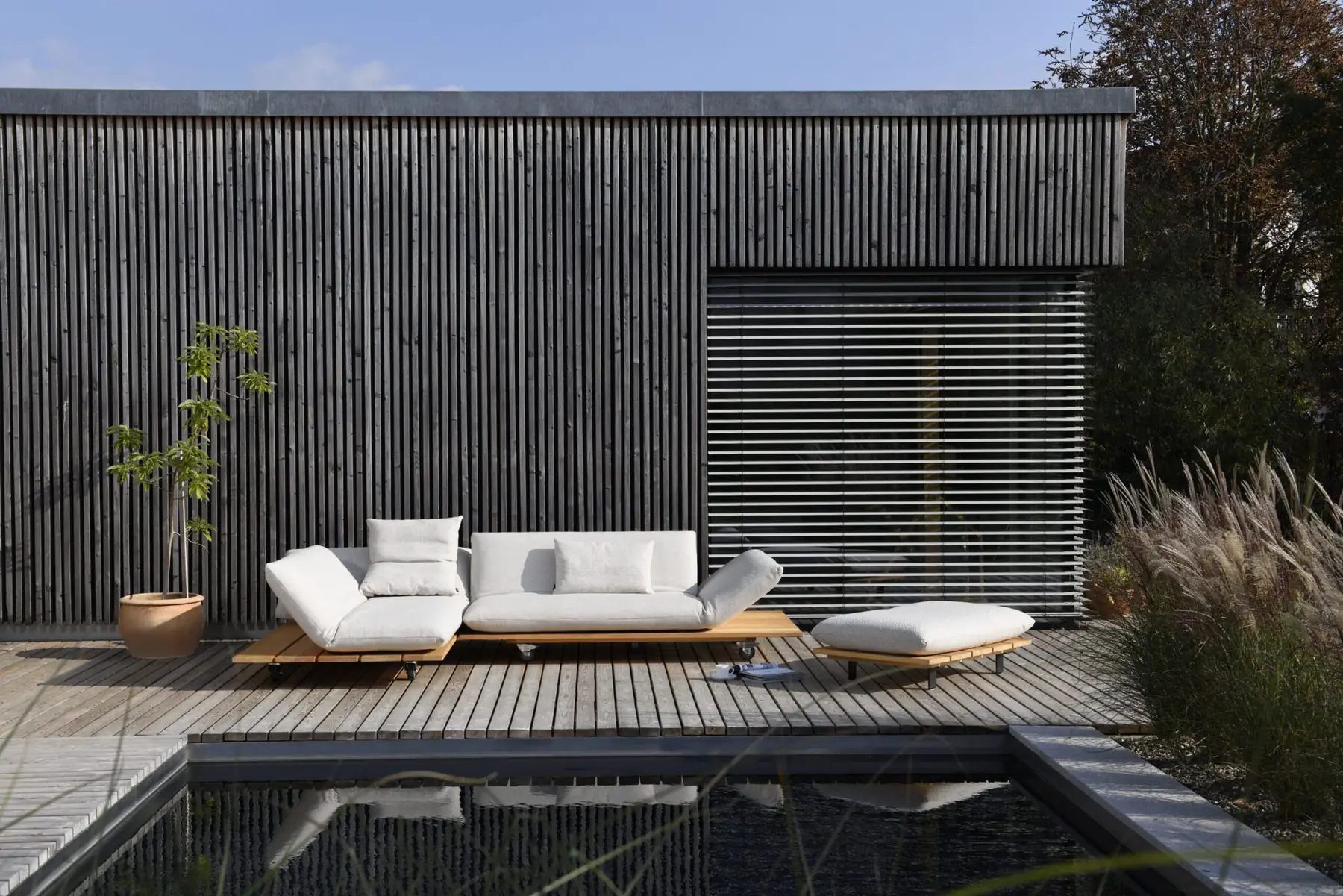 Outdoor-Liege und Hocker Akito auf einer Holzterrasse am Pool