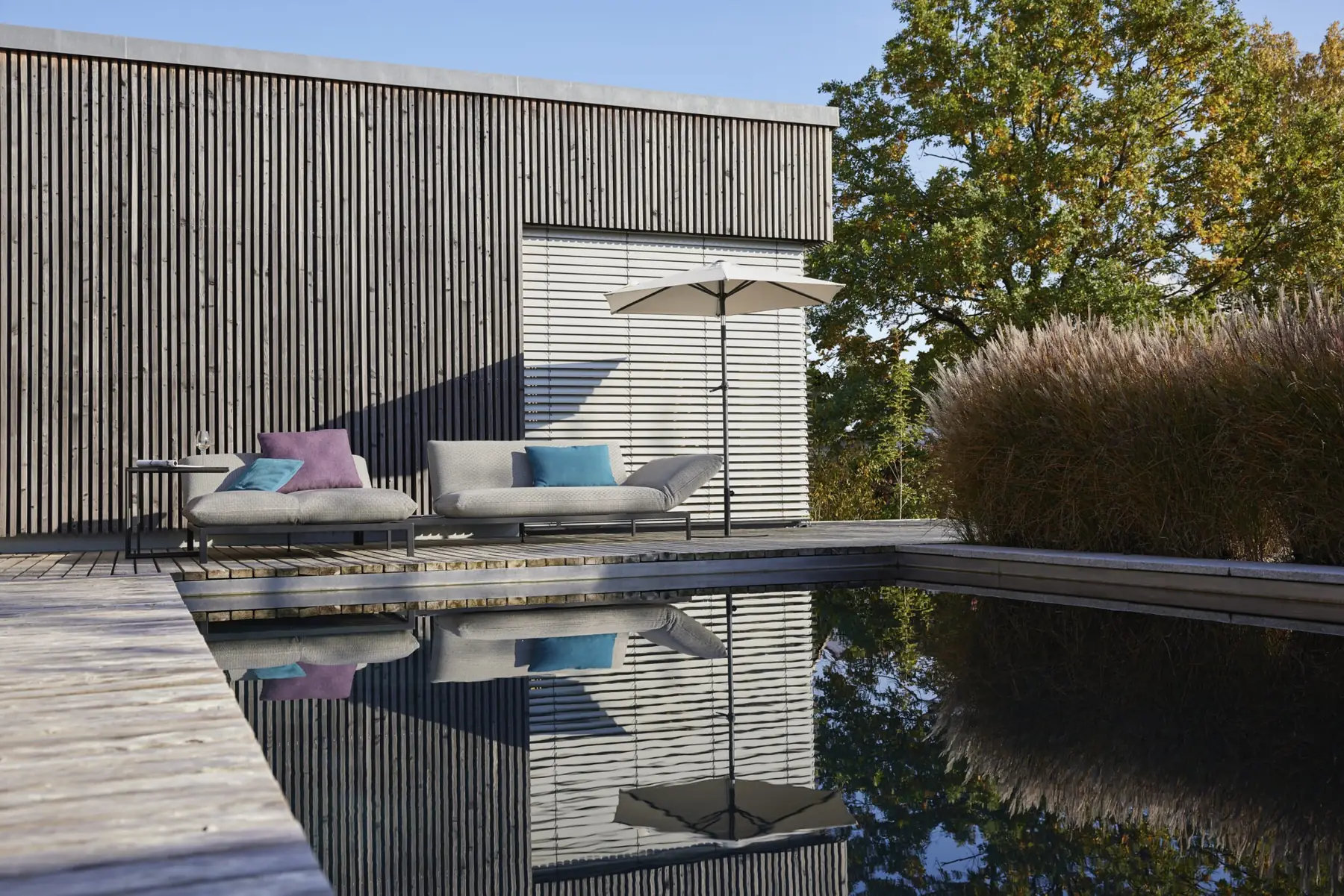 Outdoor-Möbel Kaya mit bunten Kissen und Sonnenschirm am Pool