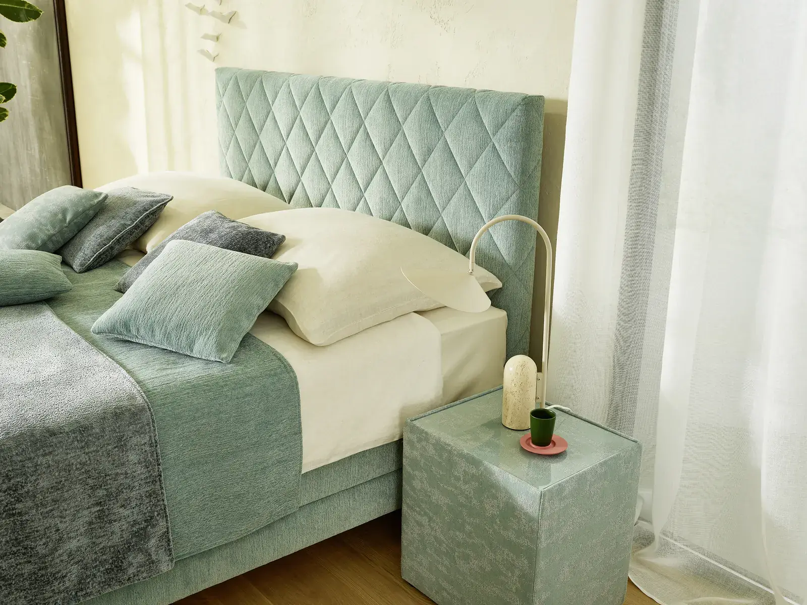 Boxspringbett mit rautenförmig abgestepptem Kopfteil und grüner Tagesdecke