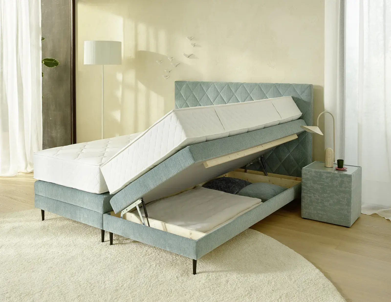 Mintgrünes Boxspringbett mit geöffnetem Bettkasten und angehobenen Liegeflächen