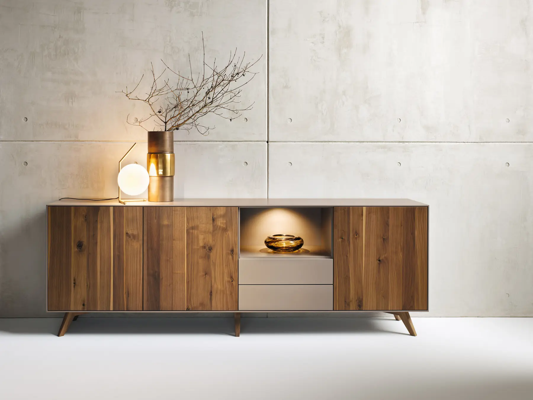 Nussbaum-Sideboard mit offenem Mittelfach und schrägen Füßen vor heller Wand