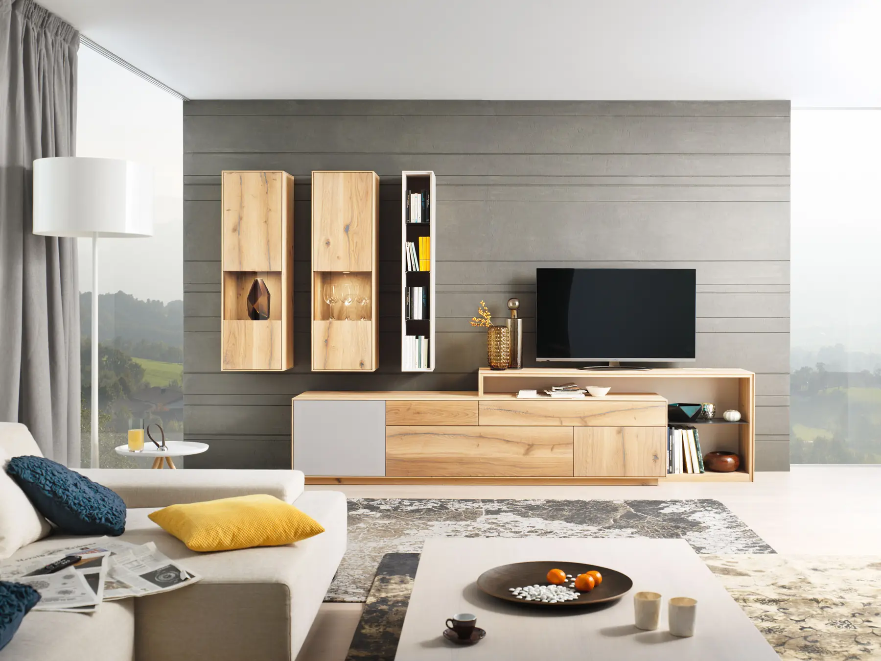 Wohnwand aus hellem Holz mit Hängevitrinen und Fernseher vor grauer Wand