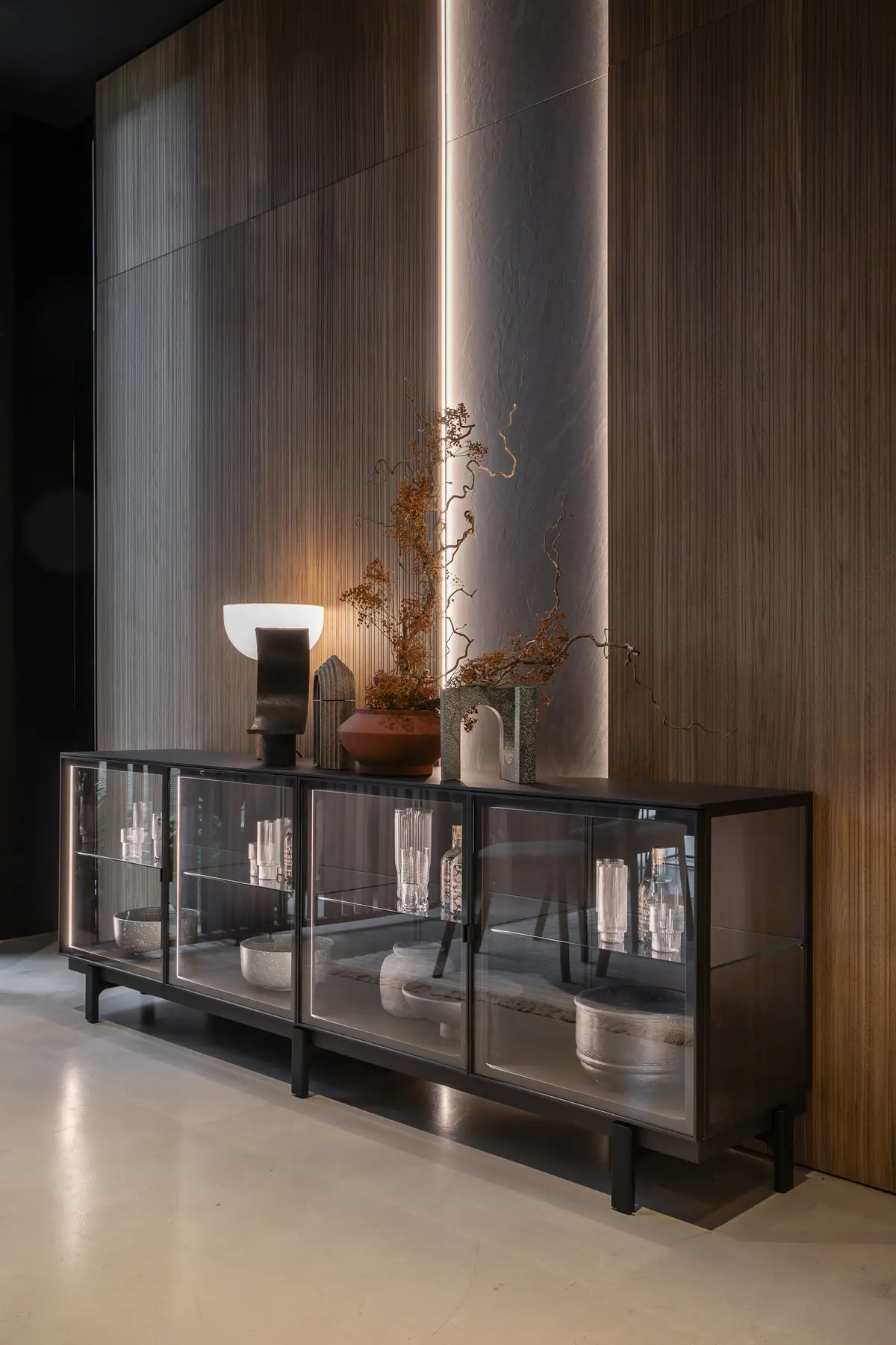 Langes dunkles Glas-Sideboard mit Geschirr vor einer Wand mit senkrechten Holzleisten