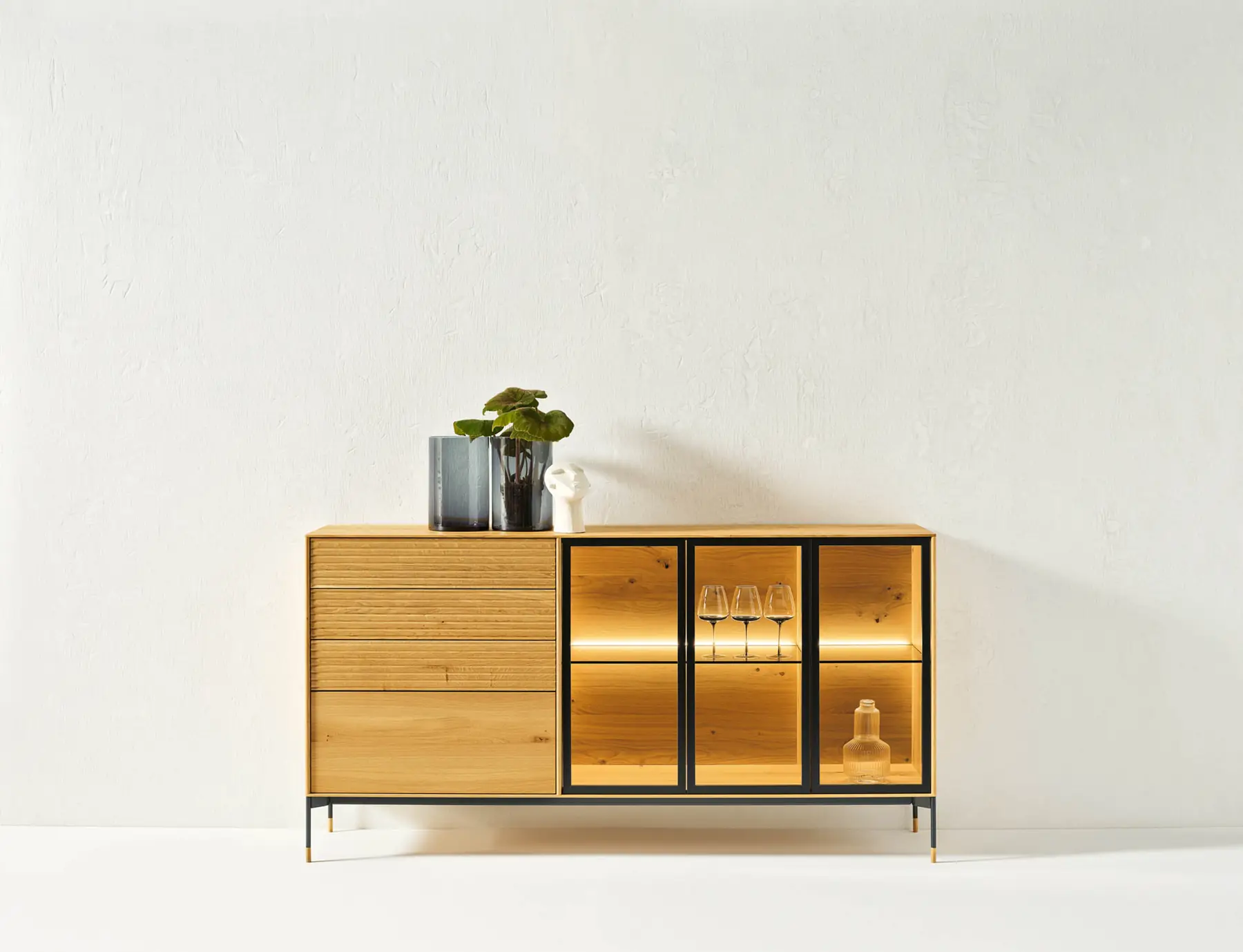 Holzsideboard mit Schubladen und beleuchteten Glasfächern auf schlankem Metallgestell