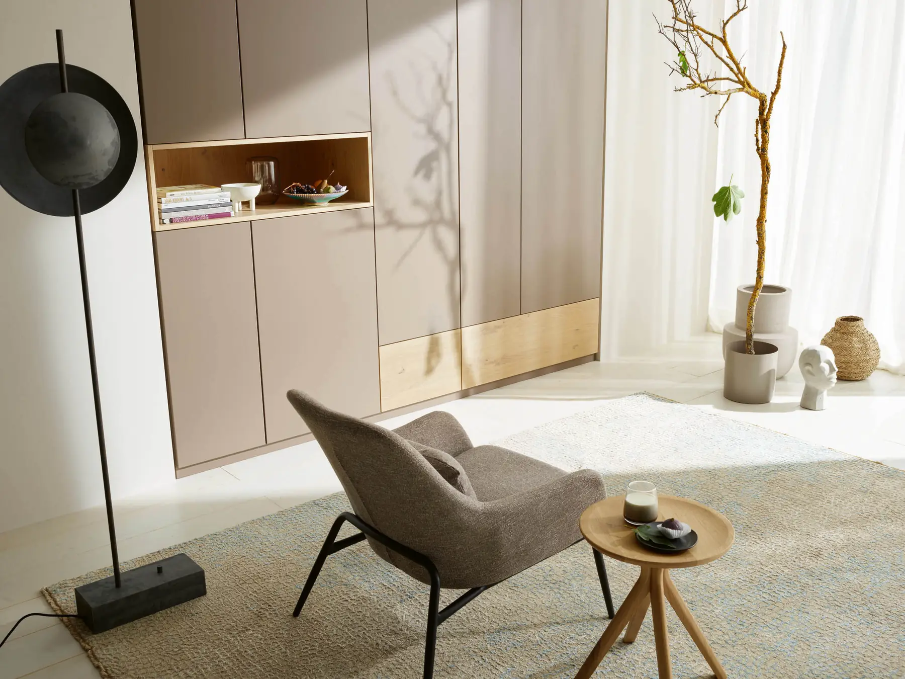 Beiger Raumschrank mit offenem Holzfach hinter einem Loungesessel mit Beistelltisch