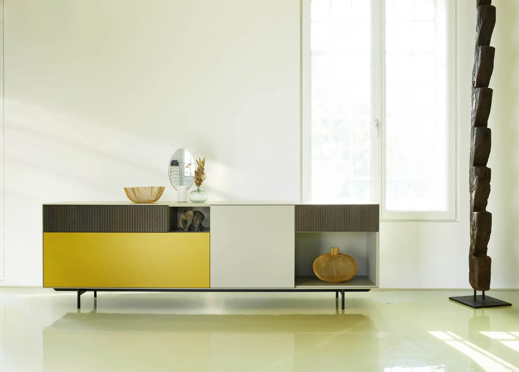 Langes Sideboard mit gelben und grauen Fronten sowie offenem Glasfach im hellen Raum