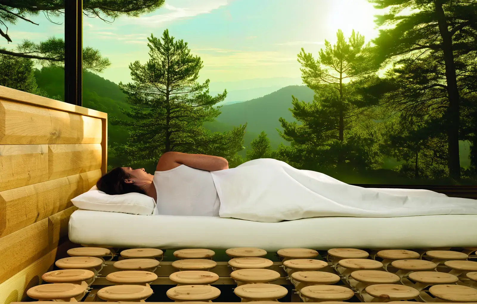 Person im Zirbenbett auf dem Relax-2000-Schlafsystem mit sichtbarem Tellersystem vor einem Waldpanorama